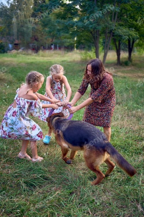 Preview: mom and little girls sisters playing with german shepherd dog during easter picnic in the garden