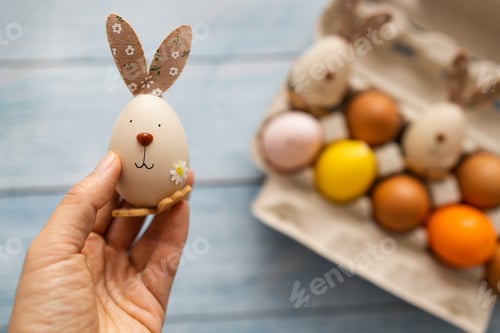 Preview: Child hands holding easter egg with funny face and bunny ears. Preparing for Easter, handmade painti