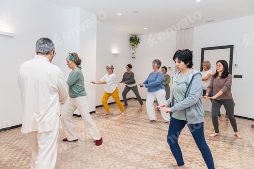 Preview: Senior women following yoga poses with focus and concentration in an indoor class