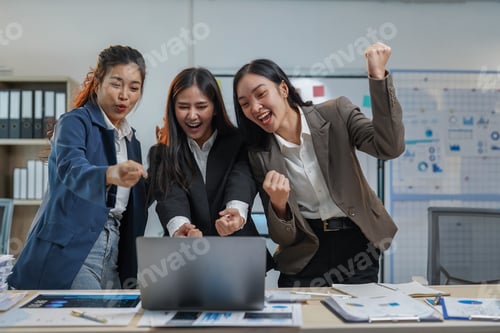 Preview: Three young businesswomen celebrating successful results in the office, joyfully engaging with a lap