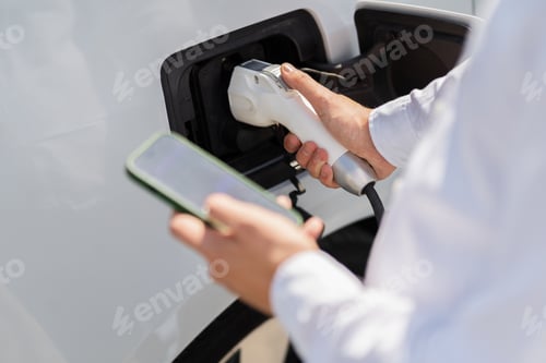 Preview: Person Charging Electric Car While Using Smartphone