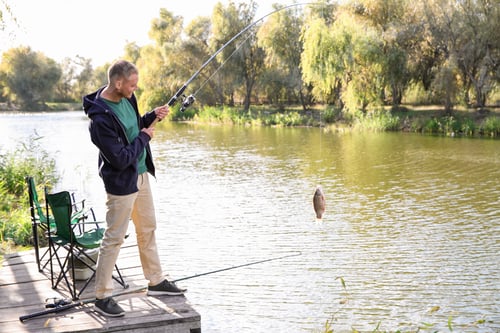 Preview: Man with rod fishing on wooden pier at riverside. Recreational activity
