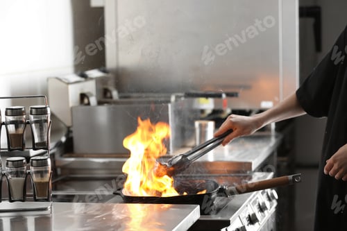 Preview: Female chef cooking meat with burning flame on stove in restaurant kitchen, closeup