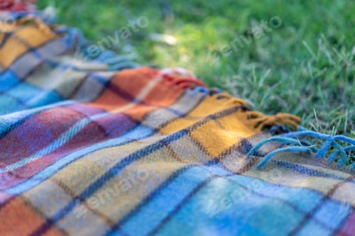 Preview: Picnic blanket lies on the grass on a sunny day. Wool checkered picnic blanket