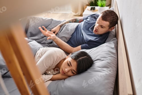 Preview: high angle view of irritated man quarreling at upset asian wife on bed at home, divorce concept