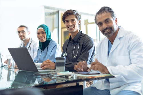 Preview: Diverse medical team looking at camera while working together at desk in hospital.