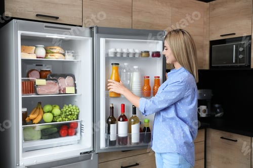 Preview: Woman taking bottle with juice out of refrigerator in kitchen