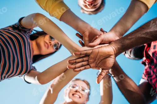 Preview: bottom view of multiracial young friends holding hands together with blue sky on backdrop