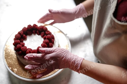 Preview: Female Chef Decorating Cake with Raspberries in Pastry Store Kitchen