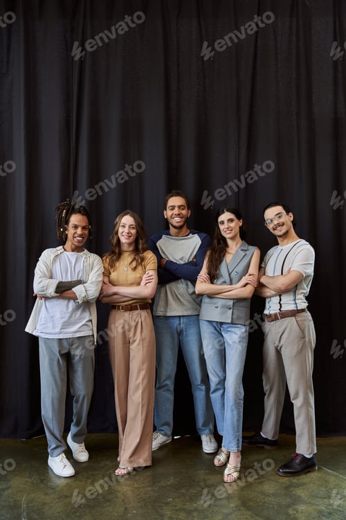 Preview: smiling multicultural team in stylish casual attire with folded arms near black drape in office