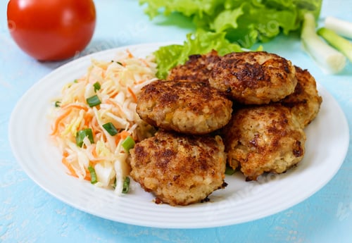 Preview: Juicy cutlets and salad with fresh vegetables: cabbage, carrots, greens on a white plate.