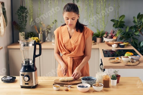 Preview: Brunette woman cutting banana by kitchen table