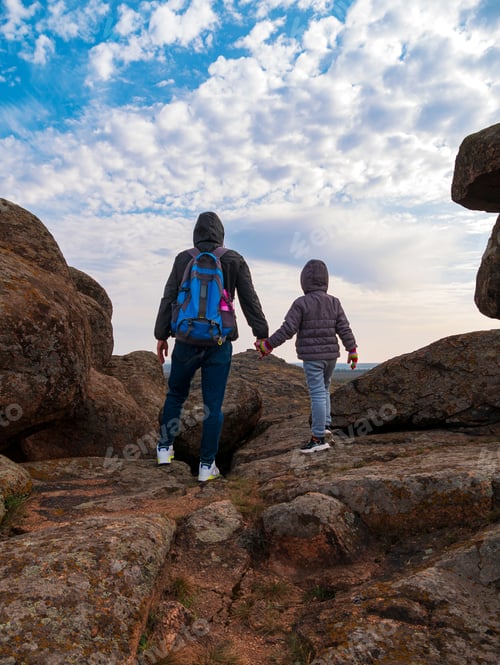 Preview: Travelers father and daughter walking climbing mountain summit blue cloudy sky back view together.