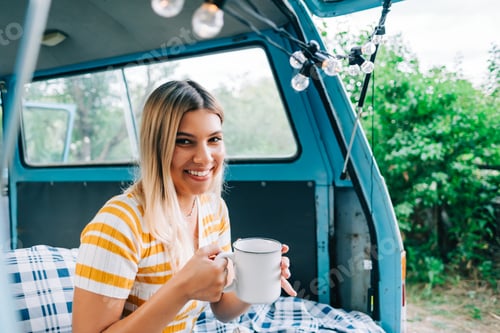 Preview: Portrait of happy young woman sitting in a van and drinking tea outdoors in nature