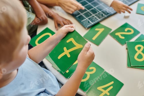 Preview: top view of boy holding number seven card, learning how to count in Montessori school, study