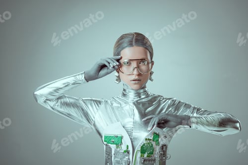 Preview: young woman robot in futuristic eyeglasses looking at camera isolated on grey, future technology