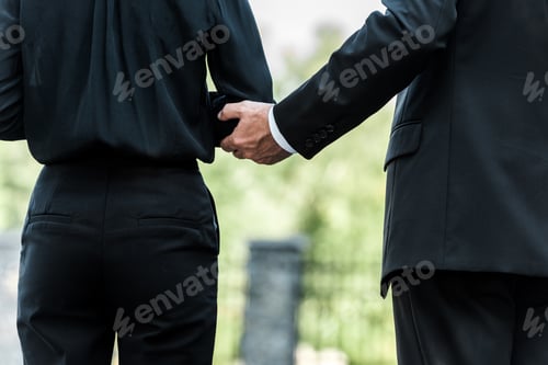 Preview: cropped view of man touching hand on woman standing on funeral