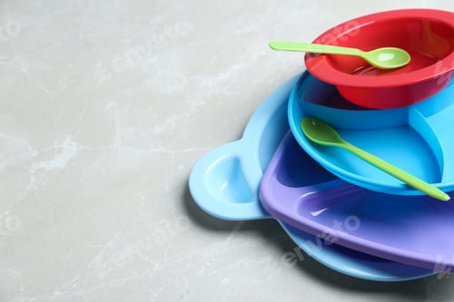 Preview: Pile of colorful plastic dishware on light grey marble table, space for text. Serving baby food