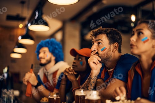 Preview: Sports fan and his friends watching football match on TV during the world cup in a bar.