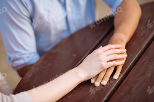 Preview: Cropped view of couple holding hands at table