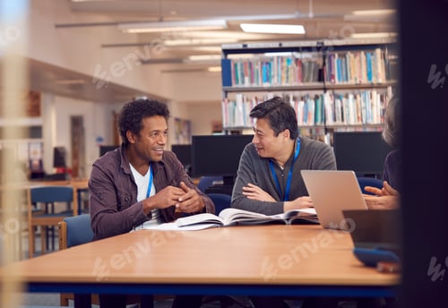 Preview: Teacher With Mature Male Adult Student Sitting At Table Working In College Library