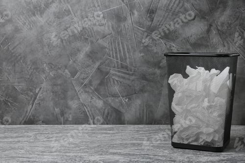 Preview: Trash bin with used toilet paper on floor near grey wall. Space for text
