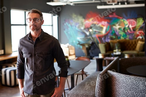 Preview: Middle aged white male creative standing in casual office canteen, cafe area looking to camera