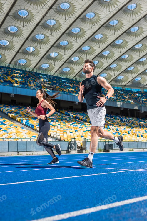 Preview: athletic young male and female joggers running on track at sports stadium