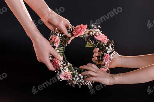 Preview: partial view of mother and daughter holding flowers wreath isolated on black