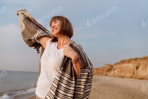Preview: Senior european woman smiling while walking on beach