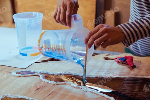 Preview: Closeup of carpenter pouring liquid epoxy in a wooden table