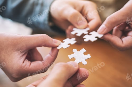 Preview: Closeup image of people's hands holding and putting a piece of white jigsaw puzzle together