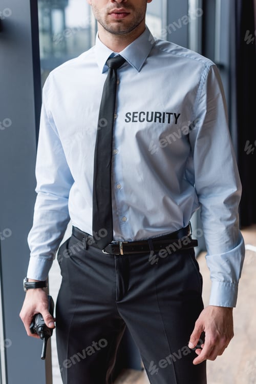 Preview: partial view of handsome guard in suit holding walkie-talkie