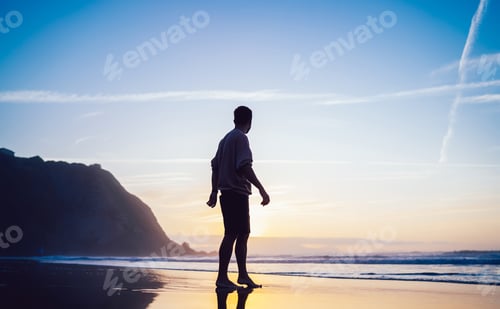 Preview: Unrecognizable man standing on sea beach looking at sunrise