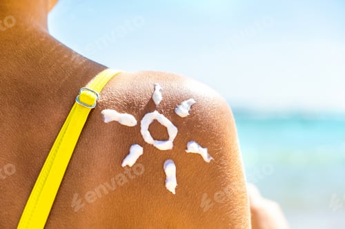 Preview: Back view of young woman tanning at the beach with sunscreen cream in sun shape