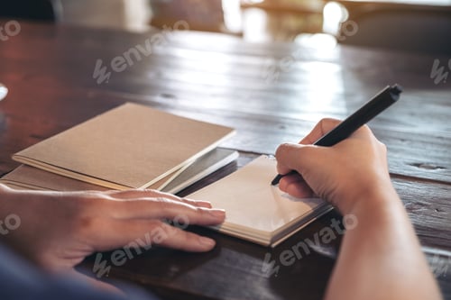 Preview: Closeup image of a woman writing on blank notebook on table in cafe