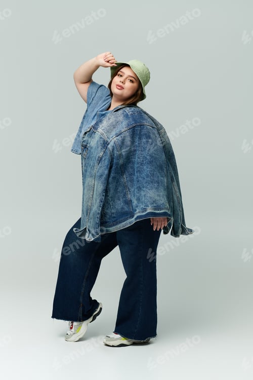 Preview: Stylish young plus size woman poses confidently in casual denim attire against a simple backdrop