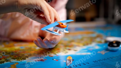 Preview: Closeup of little boy playing with small toy airplane on big world map. Concept of travel, tourism