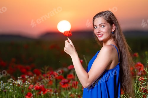 Preview: beautiful young woman playing with sun ball while standing in poppy field in warm sunset light