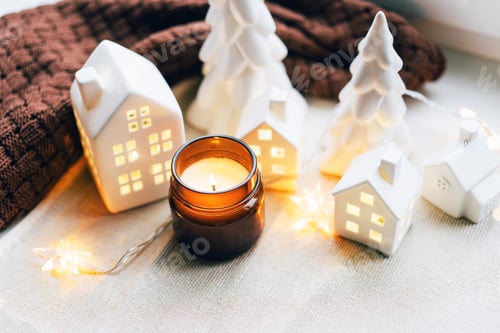 Visualização: Cena de Natal aconchegante com casas de cerâmica e luz de velas perto de uma janela