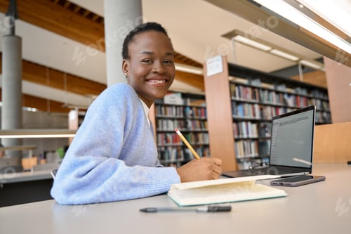 Preview: Happy African girl student using laptop learning online in library. Portrait