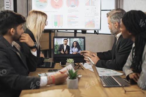 Preview: Focused multiracial business people in conference room, looking at a laptop, having video conference