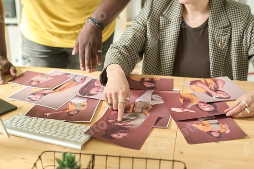Preview: Close-up of designer pointing at photo sitting at table, she choosing photos together with editor