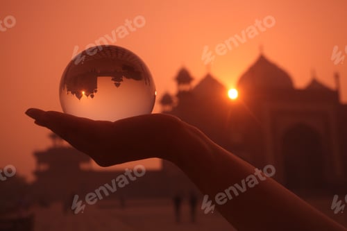 Preview: Silhouette of a person holding a glass ball with the reflection of Taj Mahal in India during sunset