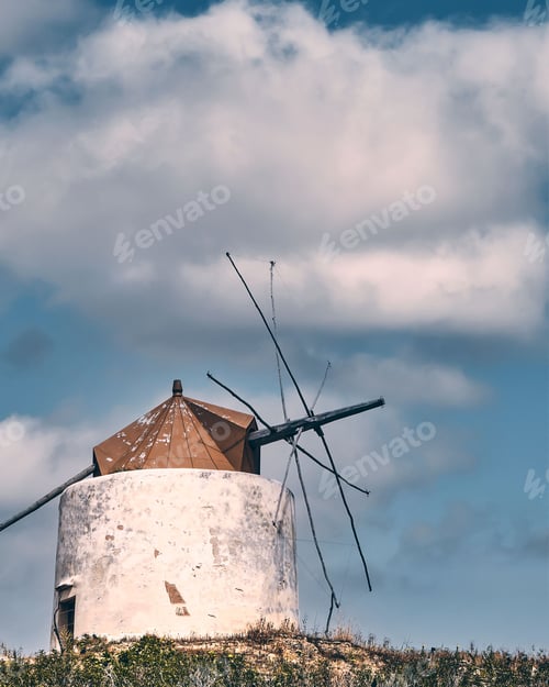 Preview: Old abandoned mill on a hill in the countryside under blue sky with white clouds