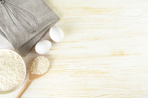 Preview: Baking ingredients flour, eggs and whisk on white wooden background with copy space