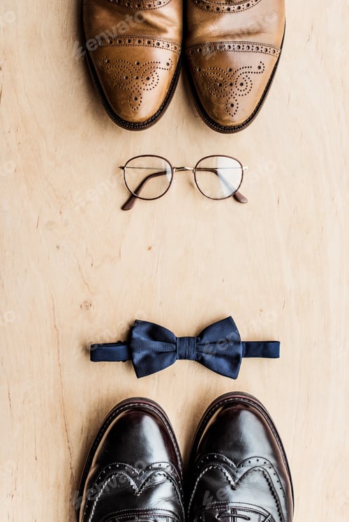Preview: top view of shoes, glasses and tie bow on wooden surface