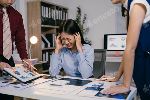 Preview: Asian businesswoman suffering from headache while working on financial report with colleagues in off
