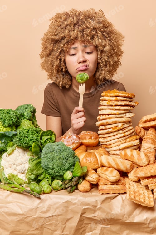Preview: Displeased curly woman looks sadly at green brussel cabbage doesnt want to eat vegetables keeps to