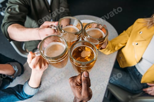 Preview: cropped shot of group of friends clinking mugs of beer